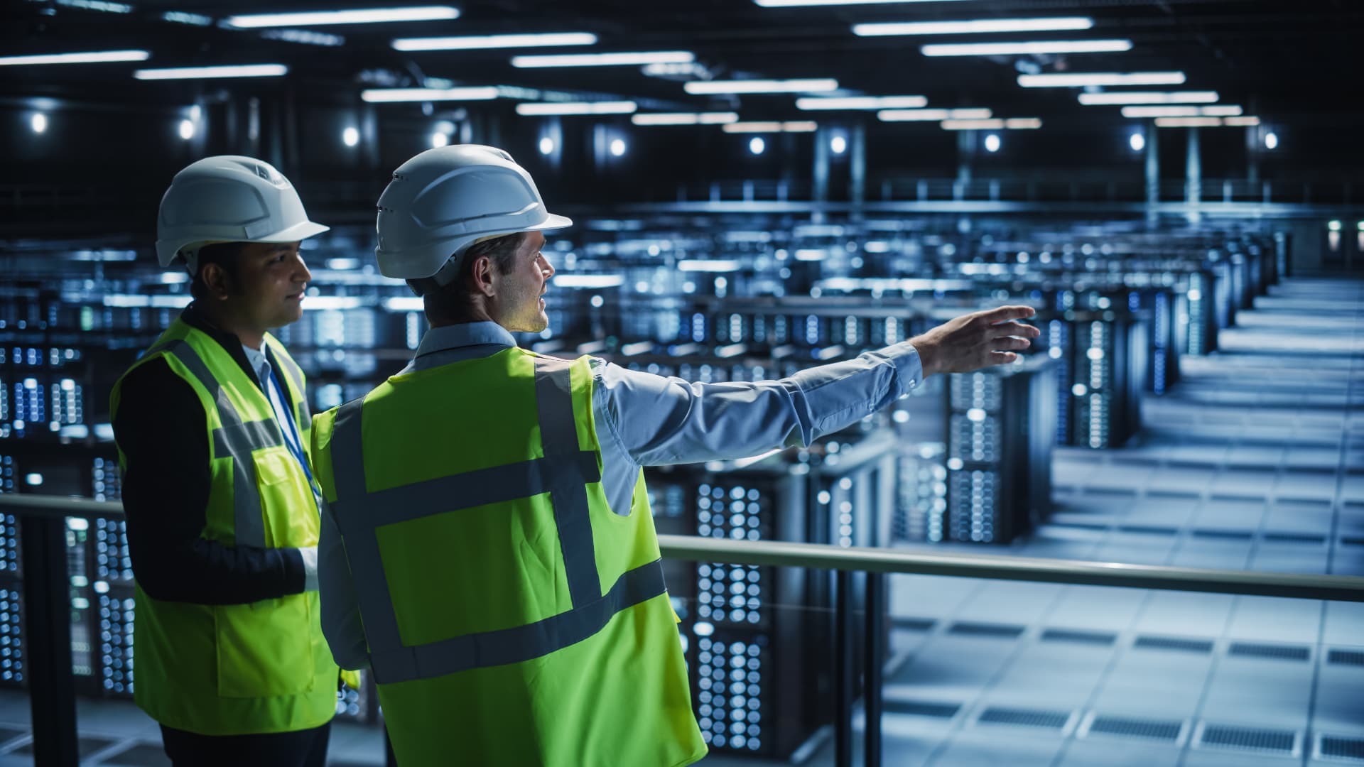 Safety professionals in hard hats observing work inside a data center server hall